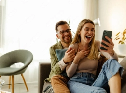 Pareja relajada en el sofá, riendo al ver algo en el teléfono