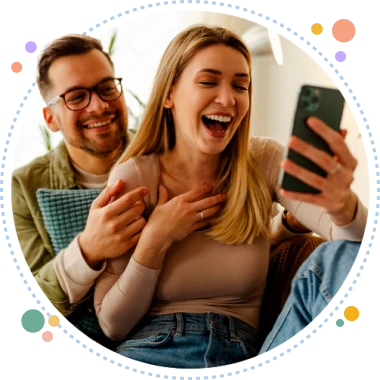 Pareja sentada en un sofá riendo mientras mira el celular